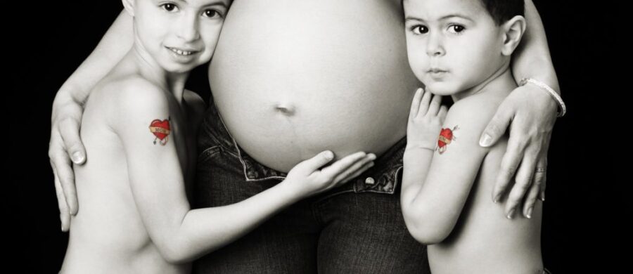 Pregnant woman with two children hugging belly.